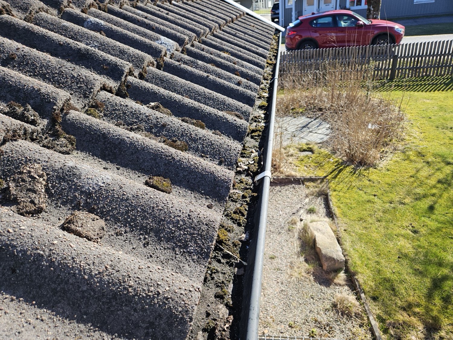 Närbild på vittrade betongpannor med mossa och grus i hängrännan
